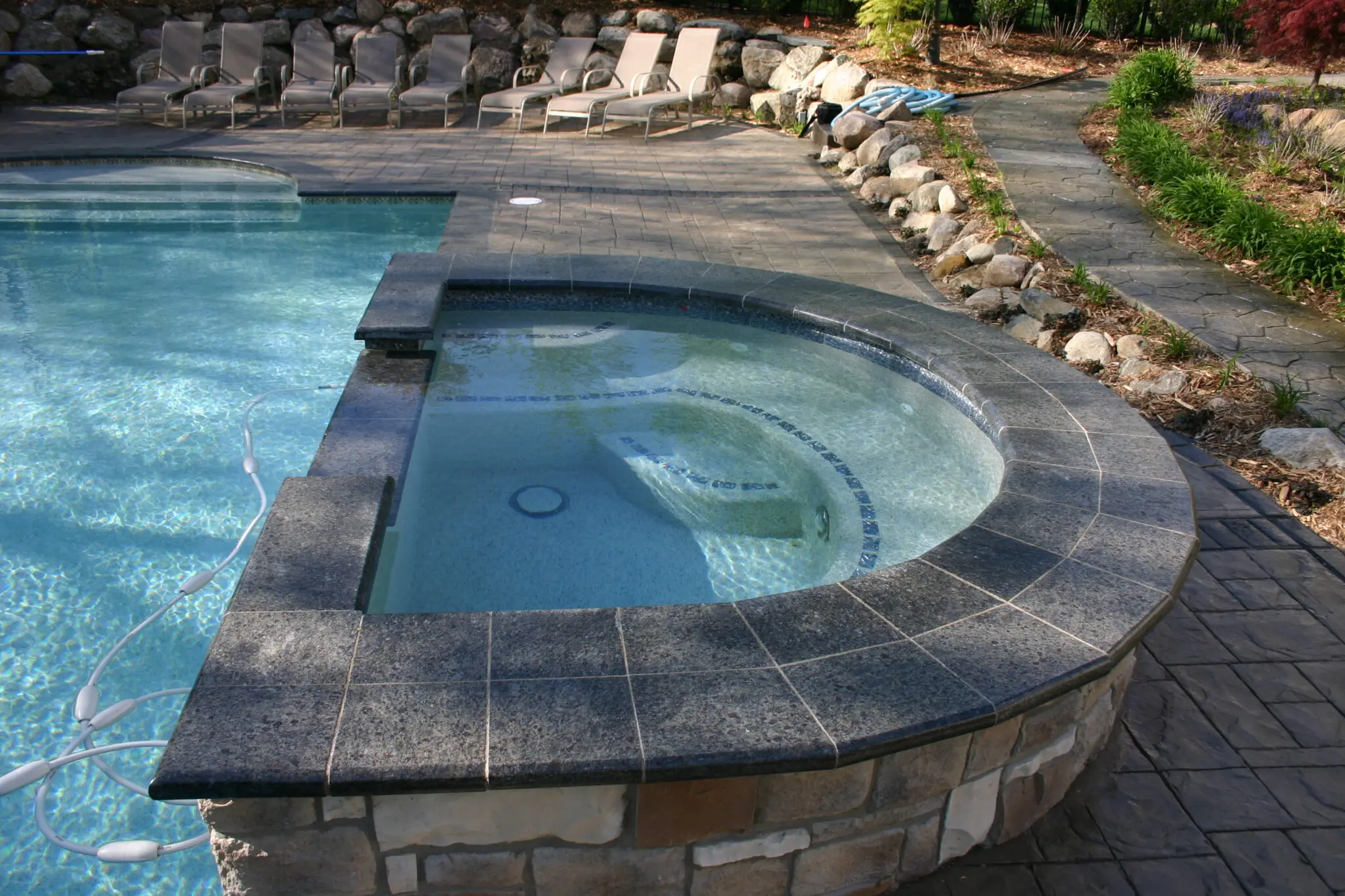 67a269a5546e4_tom pool 014 A pool with a stone wall and a large concrete slab.