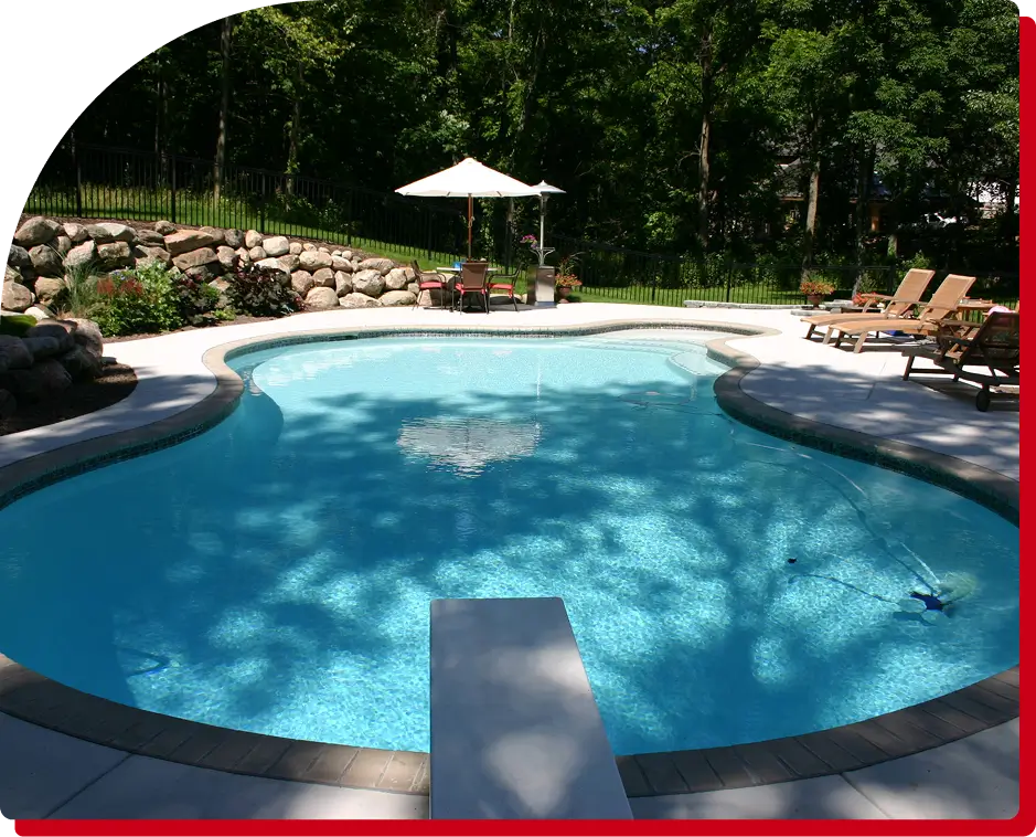 A pool with an umbrella and chairs in the background.