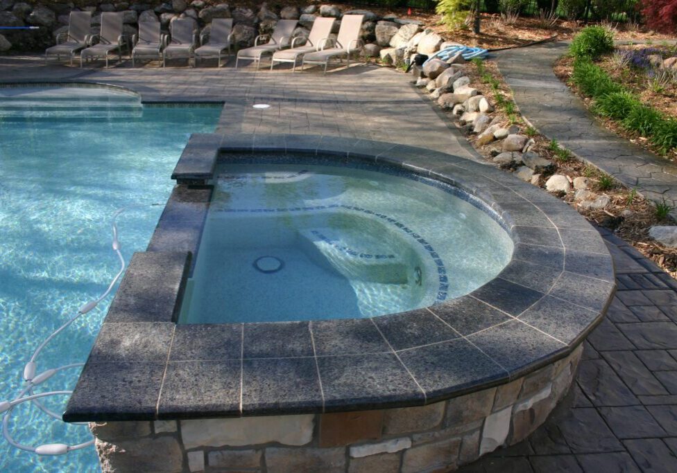 A pool with a stone wall and a large concrete slab.